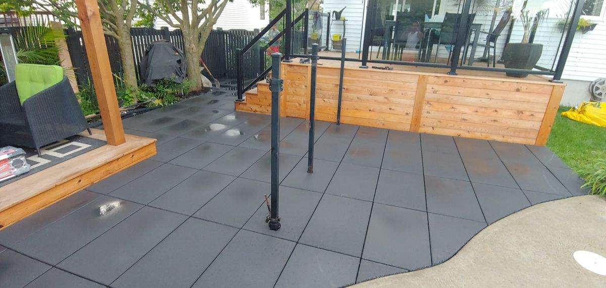 Patio en dalles foncées et terrasse en cèdre avec garde-corps en verre, près de la piscine