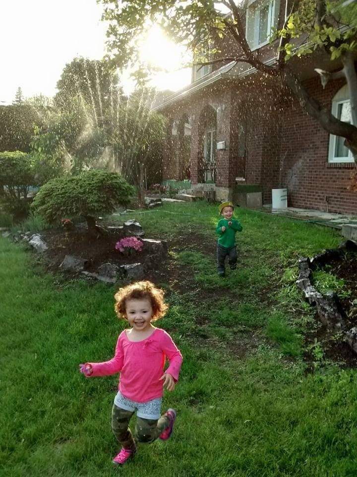 Enfant qui court dans l'arroseur dans une cour, l'été