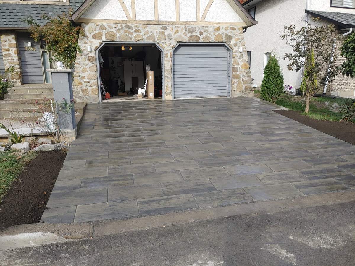 Entrée de cour en pavé gris devant une maison en pierre